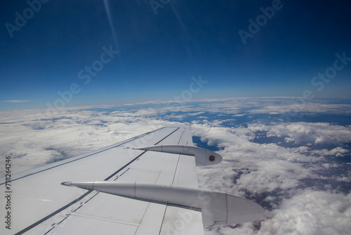 Aerial view by the airplane wing while flying above the clouds with a blue sky in the background, wide angle shot