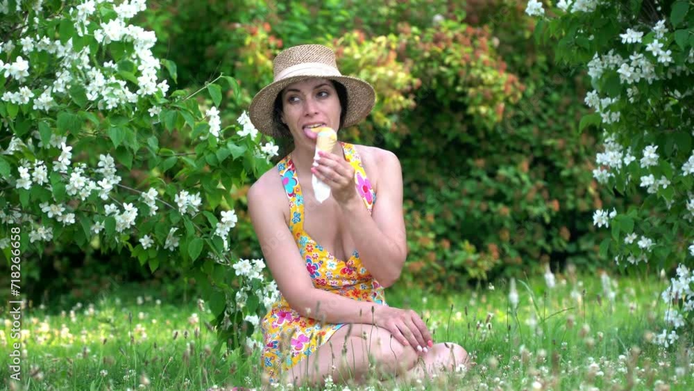 a girl in a colored dress and hat sits on the grass and eats ice cream. a girl in a colored dress and hat sits on the grass and eats ice cream.