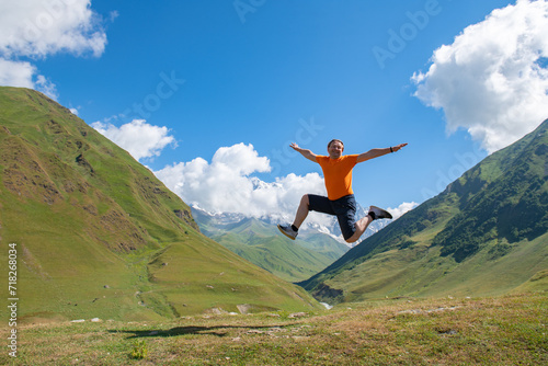 Leap into Serenity: Man Jumps amid Green Mountains and Dreamy Clouds