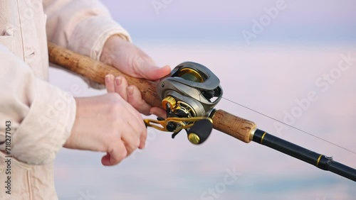 Reel of fishing rod hand rotation of orange sunset slow motion. Woman hobby fishing on sea tightens fishing line reel fish summer. Calm surface sea. Go Everywhere. Lifestyle photo