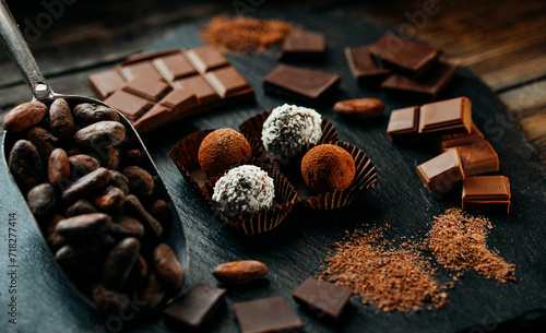Four handmade chocolate candies on spatula on blackstone stand in heart shape. Closeup chocolate candies with cocoa beans, nuts around	
