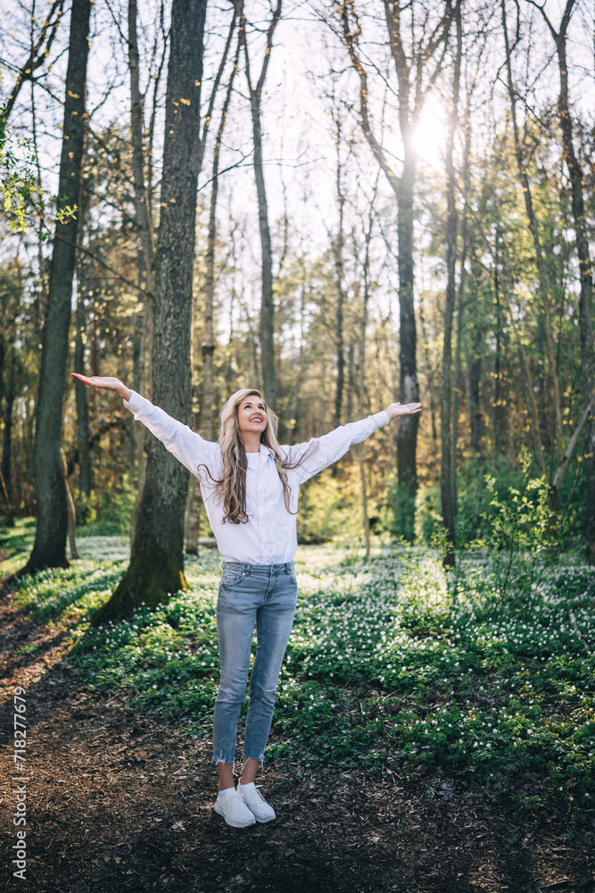 Rear view of young woman standing with open arms enjoying fresh air in spring forest. Rear view of young woman standing with open arms enjoying fresh air in spring forest.