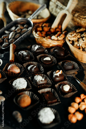 There are many chocolate candies on spatula on blackstone stand. Closeup chocolate candies with cocoa beans, nuts around