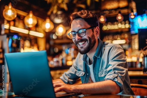 A content man, dressed in casual clothing and wearing glasses, sits comfortably indoors at a desk, his face lit up with a smile as he uses his laptop to connect with the digital world © Radomir Jovanovic