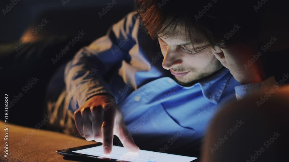 Man, tablet and reading at night for social media, research or online streaming at home. Young male person lying in relax with technology in the late evening for communication, networking or app Man, tablet and reading at night for social media, research or online streaming at home. Young male person lying in relax with technology in the late evening for communication, networking or app
