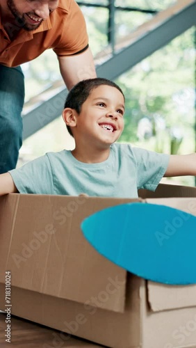 New home, father and pushing happy child in box, family having fun together or moving in house. Real estate, dad and kid in cardboard, playing game and smile in celebration for relocation in property photo