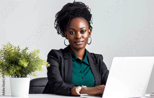 A focused woman sits at her desk, typing away on her laptop as the soft glow of the computer screen illuminates her determined expression, while a wall of framed memories stands behind her, reflectin photo