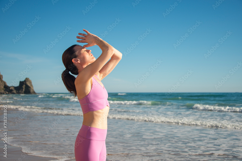 woman standing on rocks by the sea meditating and practicing yoga, arms above head woman standing on rocks by the sea meditating and practicing yoga, arms above head