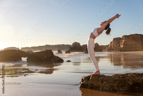 woman standing on rocks by the sea doing a backbend  yoga pose.