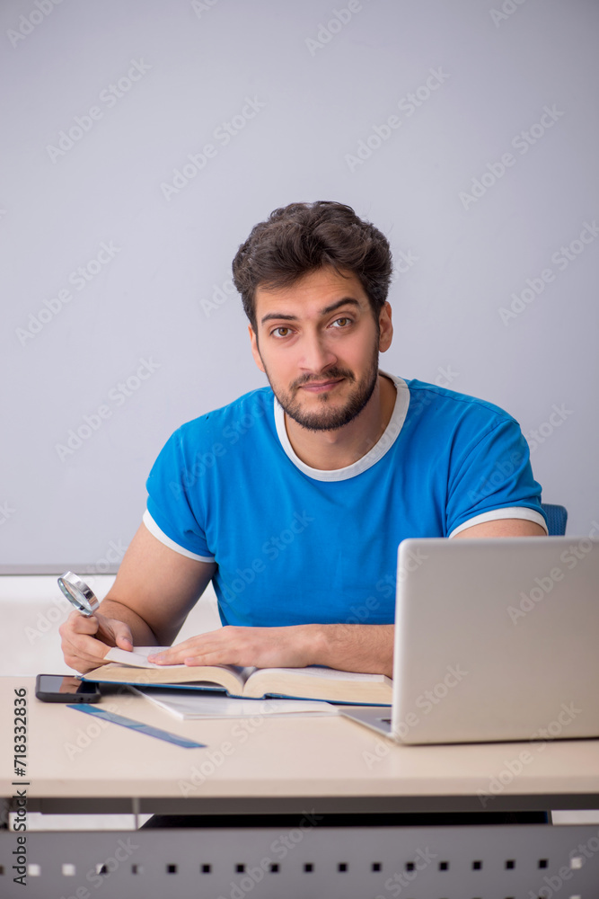 Young male student holding loupe in the classroom Young male student holding loupe in the classroom