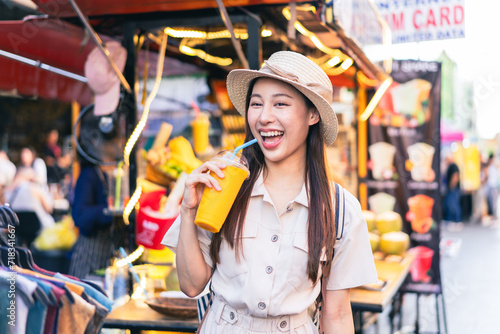 Young Asian woman traveler tourist buying a freshly made juice and walking at outdoor market in Bangkok in Thailand. People traveling, summer vacation and tourism