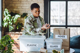 Young university student is managing waste sorting at home, smiling. Recyclable materials as paper, plastic, glass. Concept of conscious lifestyle, ecological, social responsibility, care about planet