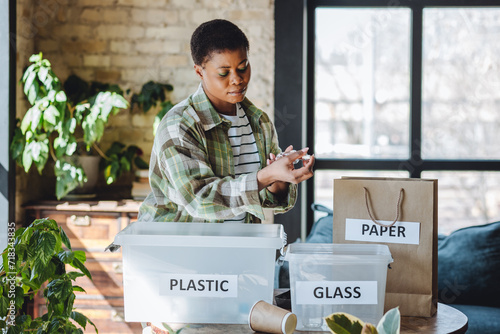 Young university student is managing waste sorting at home, smiling. Recyclable materials as paper, plastic, glass. Concept of conscious lifestyle, ecological, social responsibility, care about planet photo