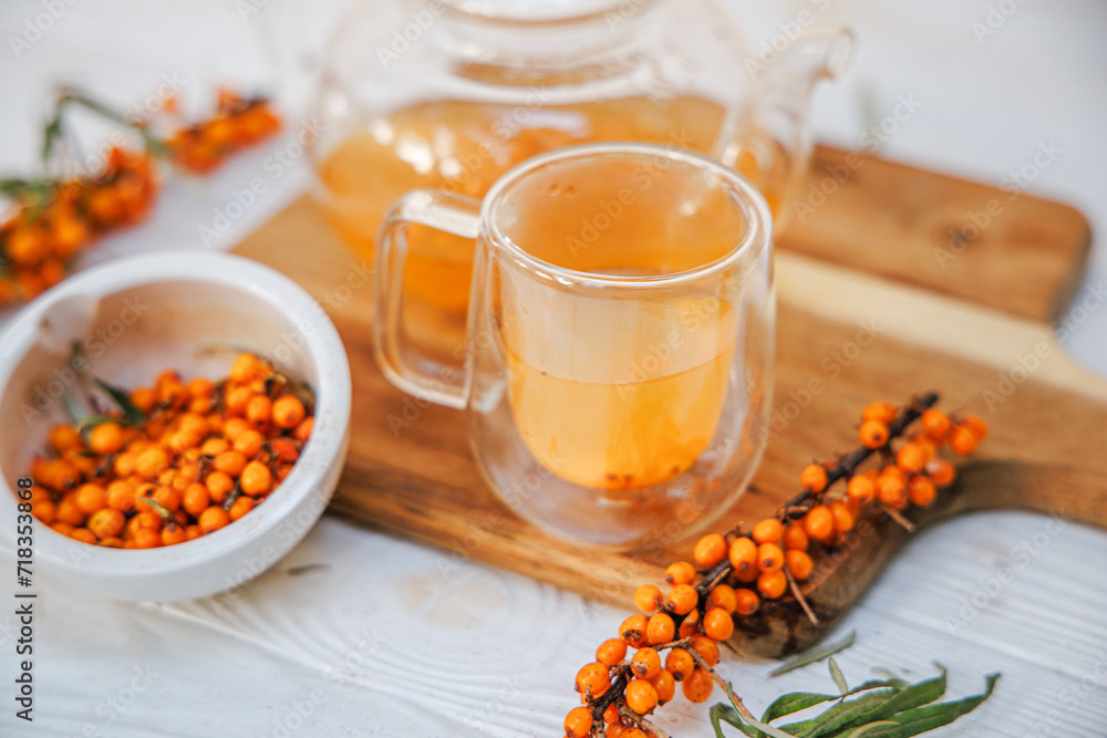 Cup with fragrant vitamin tea from sea buckthorn on a wooden table. Fresh sea buckthorn berries on a branch are ready for the preparation of a healing drink Cup with fragrant vitamin tea from sea buckthorn on a wooden table. Fresh sea buckthorn berries on a branch are ready for the preparation of a healing drink