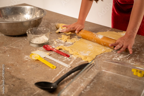 manos de niña preparando y amasando con rodillo la masa para hacer galletas con varios utensilios y recipientes para cocinar y hornear photo