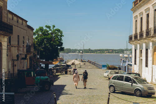woman and man walk through a coastal city with a pier and the sea in the background, Colonia del Sacramento