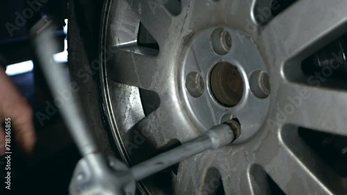 An auto mechanic at a car service center removes a car wheel. The video shows the process of unscrewing the nuts from the wheel. photo