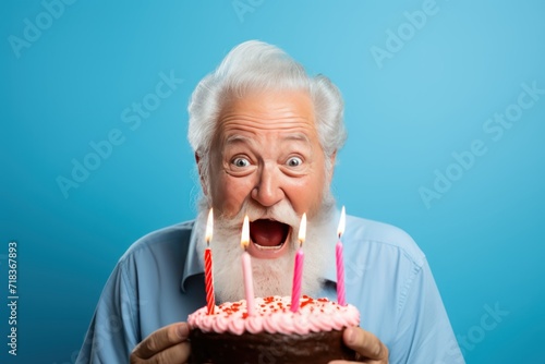 Happy senior man holding birthday cake with candles on blue background. Birthday concept with copy space. Birthday cake. Birthday Celebration.