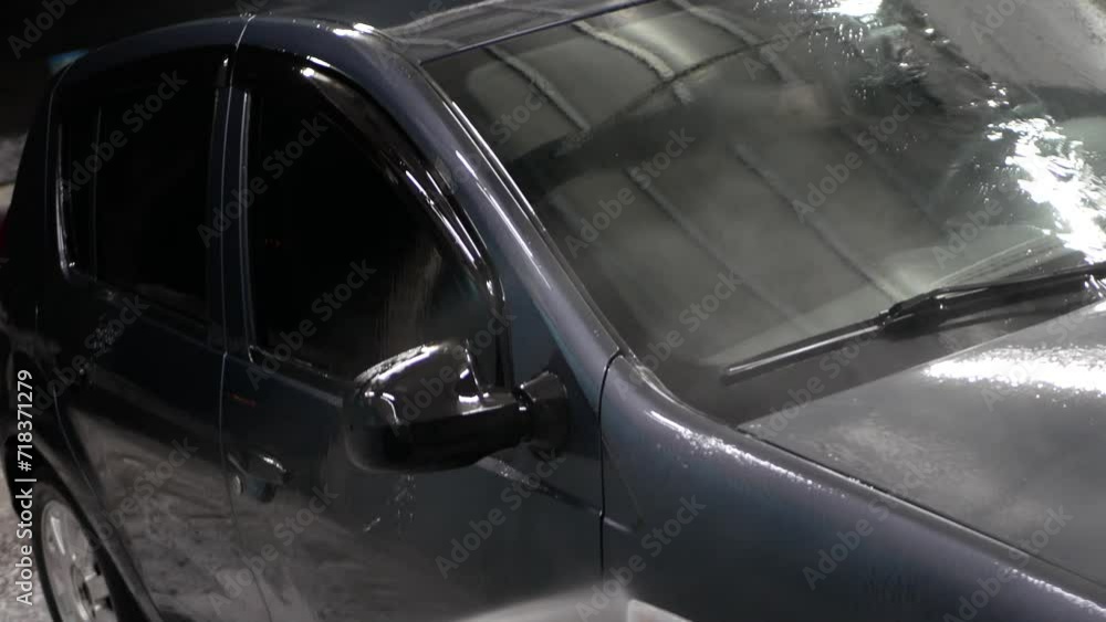 Washing a car in a car wash with high pressure water. A worker carefully washes the front of the car. Washing a car in a car wash with high pressure water. A worker carefully washes the front of the car.