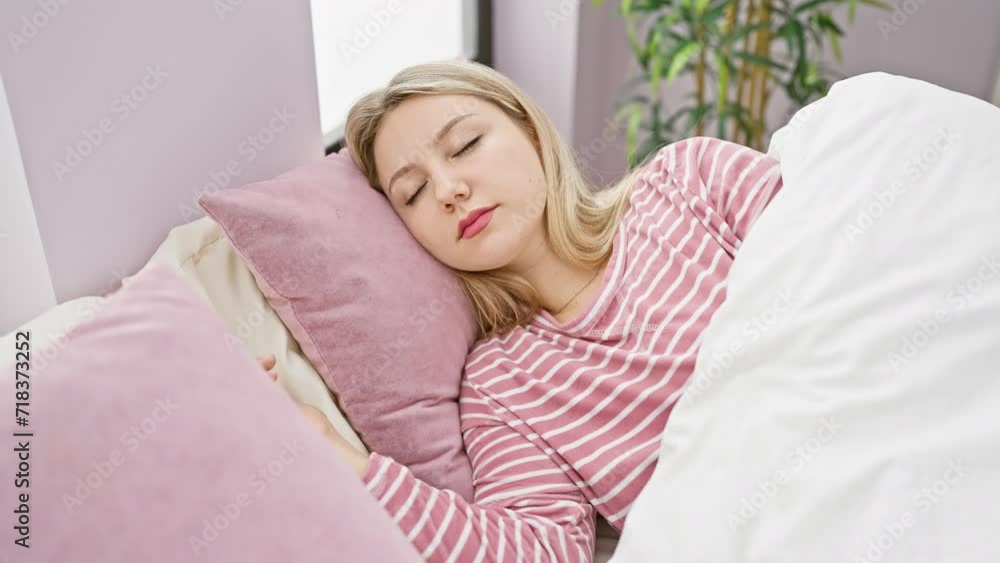 A tranquil young blonde woman peacefully sleeps in her pink-striped pajamas within the cozy ambiance of a bedroom setting. A tranquil young blonde woman peacefully sleeps in her pink-striped pajamas within the cozy ambiance of a bedroom setting.