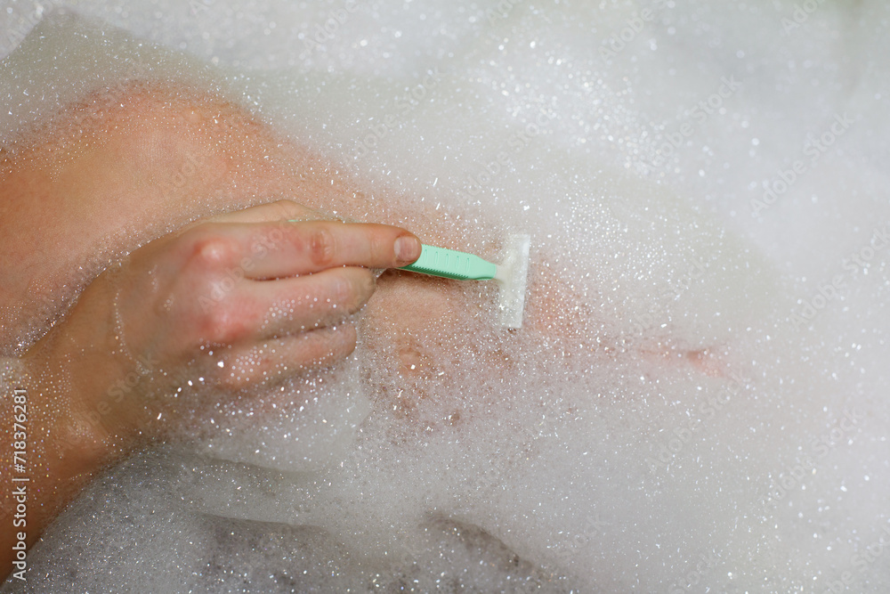 Fototapeta premium close-up woman shaving her legs in bath with foam. depilation