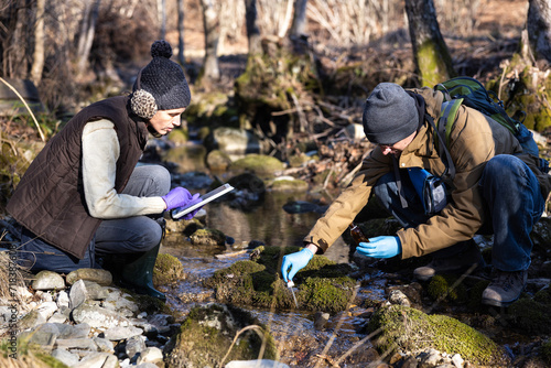 Caucasian Young Adult Biologists Collecting Water Samples from a Forest Water Stream in Winter