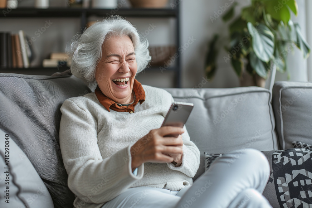 Elderly Woman Laughing While Looking at Smartphone, Comfortable Home Setting Elderly Woman Laughing While Looking at Smartphone, Comfortable Home Setting