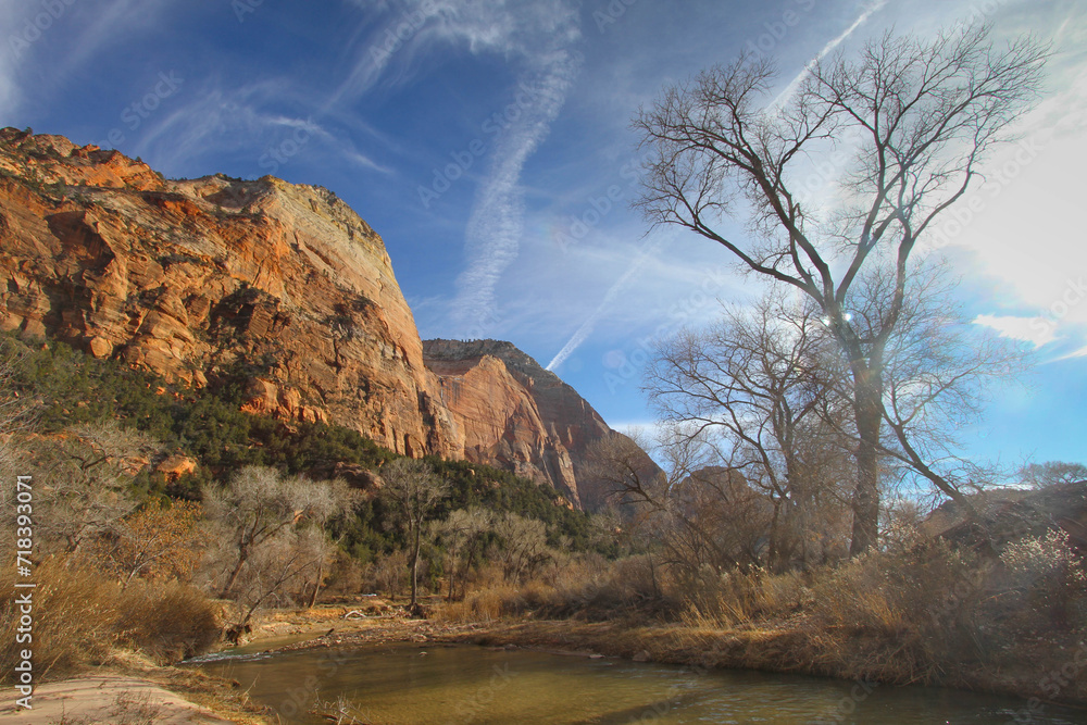 photograph of red rock bluff by a slow moving river with a very interesting sky with fluffy clouds and jet streams taken in Zions Park in Utah