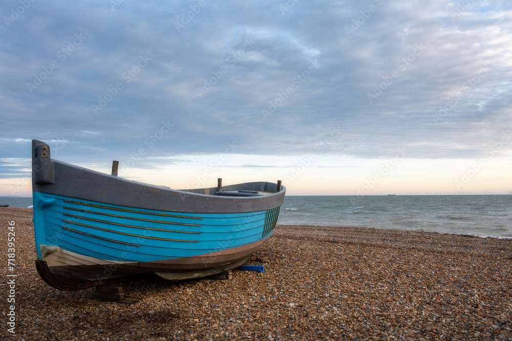Blue boat on a shingle beach on a cloudy winter day