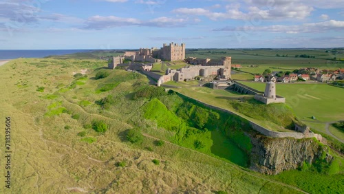 AERIAL: Beautiful view of historic Bamburgh Castle in an exceptional location. Stunning attraction with a remarkable fortress on top of a crag rising on the edge of green fields above a sandy beach. photo