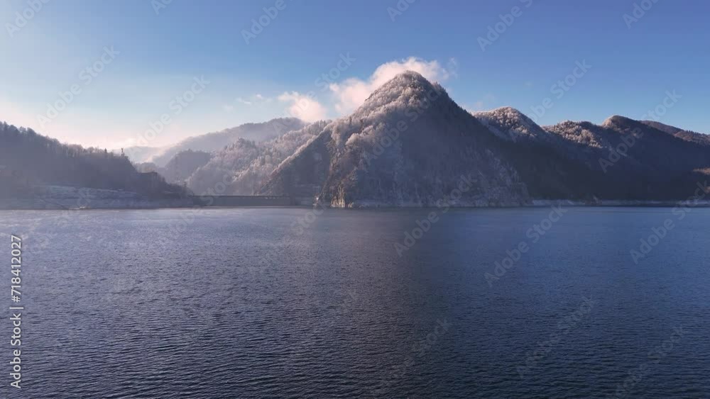 Aerial view of Water dam between snow covered mountains. Reservoir between high mountains. Hydroelectric power plant. Frozen trees in the mountain forest. Vidraru Reservoir in the Fagaras. Aerial view of Water dam between snow covered mountains. Reservoir between high mountains. Hydroelectric power plant. Frozen trees in the mountain forest. Vidraru Reservoir in the Fagaras.