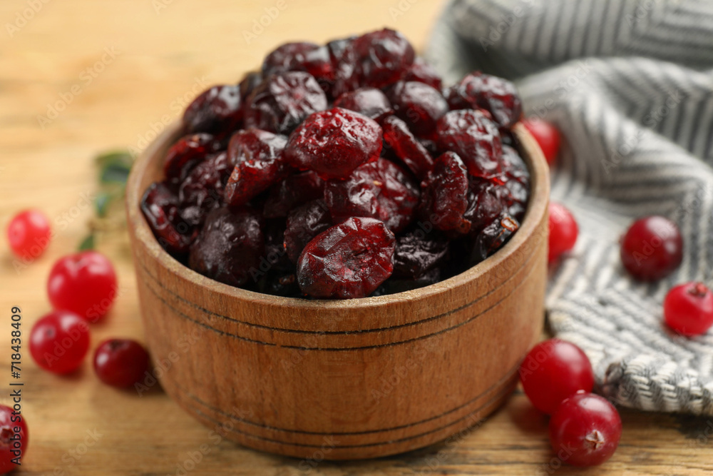 Tasty dried cranberries in bowl and fresh ones on wooden table, closeup Tasty dried cranberries in bowl and fresh ones on wooden table, closeup