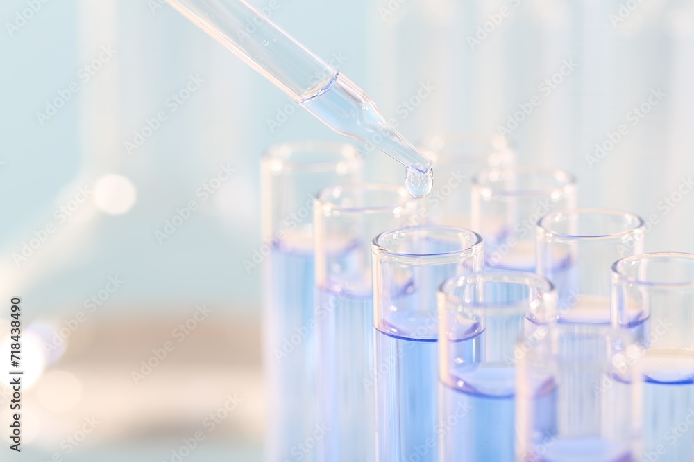 Laboratory analysis. Dripping light blue liquid from pipette into glass test tube on blurred background, closeup and space for text Laboratory analysis. Dripping light blue liquid from pipette into glass test tube on blurred background, closeup and space for text