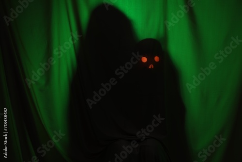 Silhouette of creepy ghost with skull behind dark green cloth photo