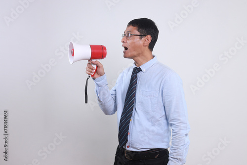 Side view of happy young man in shirt and tie using megaphone to announce good news while standing against white background
