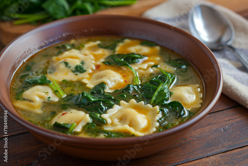 Ravioli spinach soup in brow ceramic bowl on wooden table with spoon