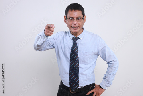 Adult Asian business man wearing glasses, shirt and tie pointing to the camera with angry expression