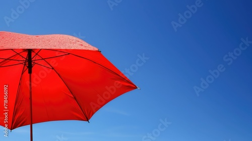 Bright red umbrella with water droplets against a clear blue sky