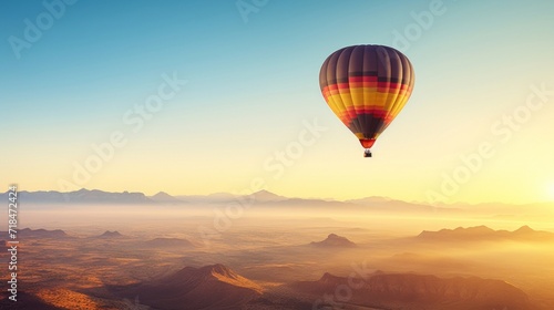 A colorful hot air balloon floats peacefully over a tranquil desert landscape at sunrise. © red_orange_stock