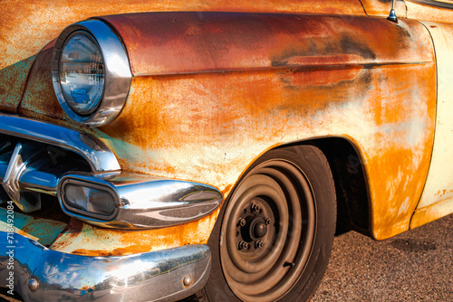 weathered, rusty, patina, left front fender of a vintage automobile, black walled tire with no hub cap, chrome headlight ring, grill, and bumper, late afternoon sun brings out warm colors photo