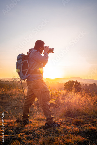  With camera and backpack, the photographer chases the golden light that caresses the mountains at dawn.adventurer concept, local travel,