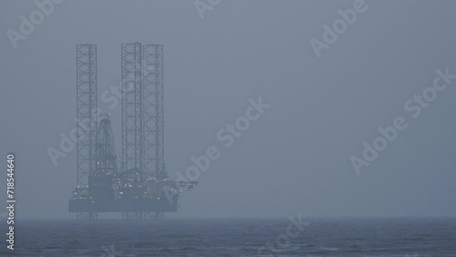 Gas rig situated off Ainsdale beach with lights on at sunset photo