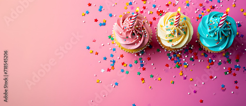 Three Cupcakes With Colorful Frosting and Sprinkles on a Pink Background
