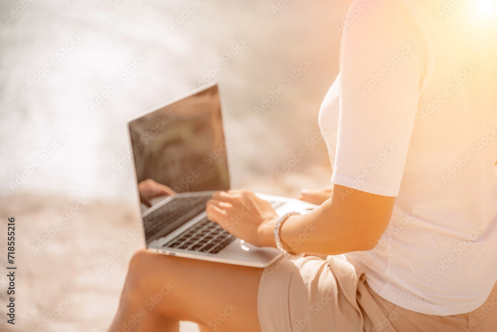 Fototapeta premium Freelance women sea working on the computer. Good looking middle aged woman typing on a laptop keyboard outdoors with a beautiful sea view. The concept of remote work.