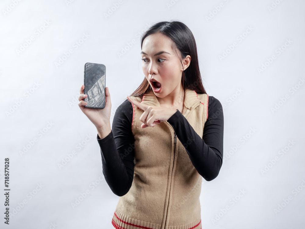 Portrait of an Indonesian Asian woman, wearing a light brown sweater, posing while showing her phone screen, isolated against a white background.
Portrait of an Indonesian Asian woman, wearing a light brown sweater, posing while showing her phone screen, isolated against a white background.