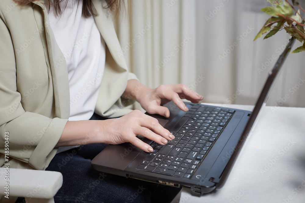 Fototapeta premium The hands of an elderly woman on a laptop keyboard. The lady communicates, works, studies on the Internet online. A businesslike old lady in modern gadget