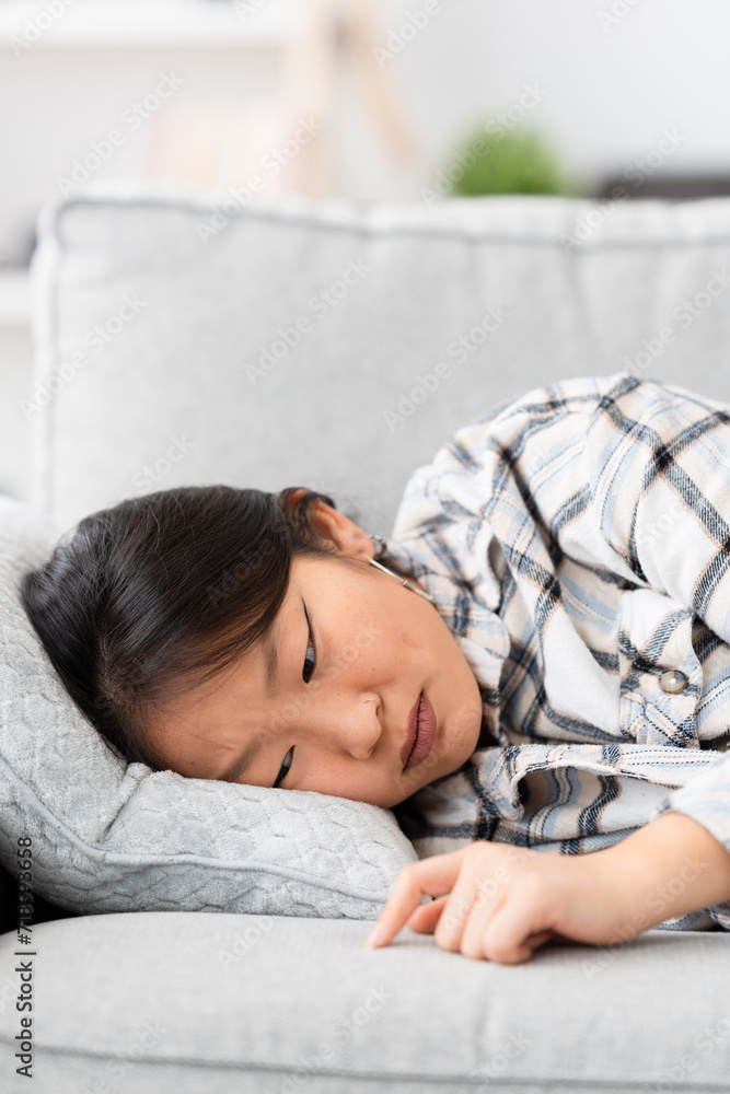 Vertical photo of a sad asian woman lying on the sofa