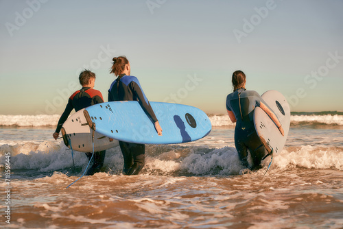 Group of surfers with surfboards in wetsuit entering towards ocean for ride the waves