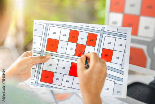 Woman holding a pencil pointing to cadastral map to decide to buy land. real estate concept with vacant land for building construction and housing subdivision for sale, rent, buy, investment. photo