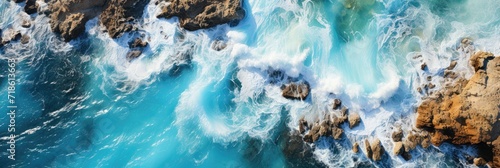 Aerial view of a rocky shoreline with the vibrant blue sea crashing onto the rocks. © AdriFerrer